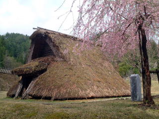 赤保木石器時代火炉の上に復元された竪穴式住居の写真