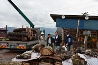 写真：運び込まれた木材を前に山崎理事長らから説明を受ける田中市長