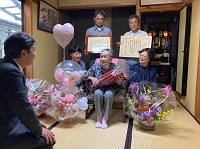 写真：ご家族に囲まれて笑顔で長寿の秘訣を話す土洞さん
