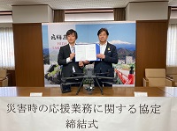 写真：締結した協定書を手にする山崎裕孝ドローンコンシェルジュ社長と田中市長