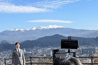 写真：冠雪した北アルプスに抱かれた市街地を望むスカイパークでの収録のようす