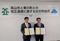 写真（右から）：締結後の協定書を手にする菊地東川町長、田中市長