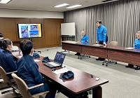 写真：記録写真とともに被災地での活動報告を受け、被災地支援に携わった職員に労いの言葉をかける田中市長