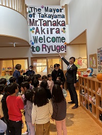 写真：保育園児の皆さんにウェルカムサインとともに迎えられる田中市長