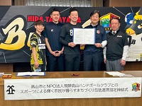 写真：締結した協定書を手にする山越雄一朗理事長、伊藤ヘッドコーチ、豊島キャプテンと田中市長