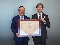 中村和男シミックホールディングス代表取締役CEOが紺綬褒章を手にし市長と記念撮影