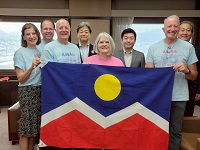 デンバー高山姉妹都市委員会のスーザン・ウェラー会長らとデンバーの市旗を手に記念撮影